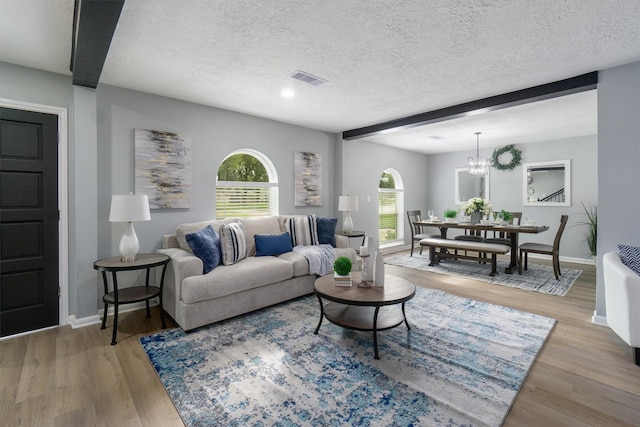 living room featuring beam ceiling, light wood-type flooring, a textured ceiling, and a chandelier