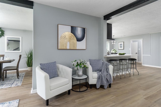 living area featuring beamed ceiling, a textured ceiling, and light hardwood / wood-style flooring