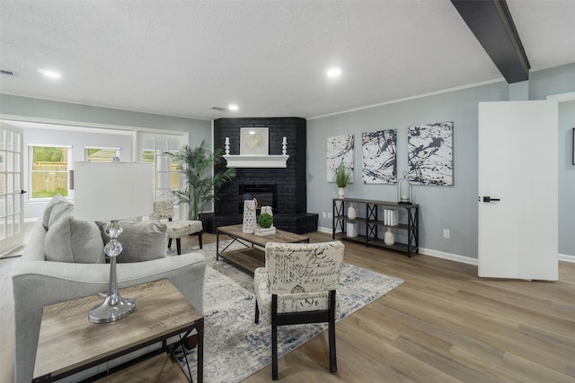 living room featuring a brick fireplace, crown molding, a textured ceiling, and hardwood / wood-style flooring