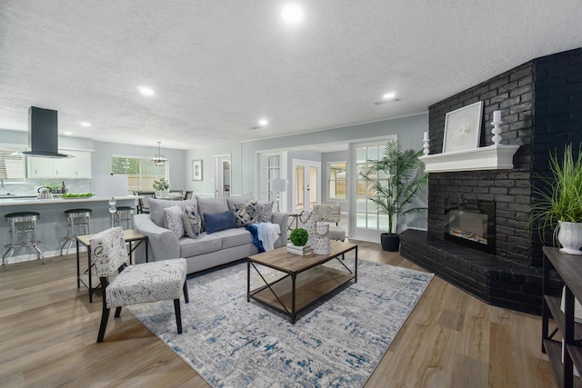 living room with light hardwood / wood-style floors, a textured ceiling, and a brick fireplace