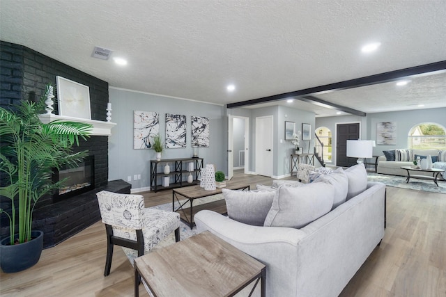 living room featuring a fireplace, beam ceiling, a textured ceiling, and light hardwood / wood-style floors