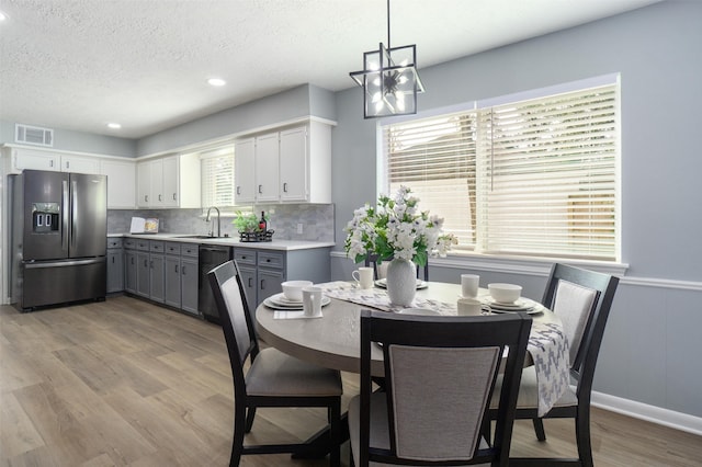 kitchen with gray cabinetry, stainless steel refrigerator with ice dispenser, hanging light fixtures, black dishwasher, and a healthy amount of sunlight