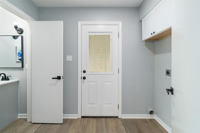 laundry room with electric dryer hookup, cabinets, and light wood-type flooring