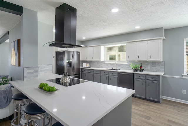 kitchen with kitchen peninsula, a kitchen bar, island exhaust hood, stainless steel appliances, and white cabinetry