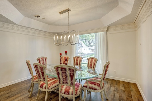 dining area with crown molding, wood-type flooring, a textured ceiling, and a tray ceiling