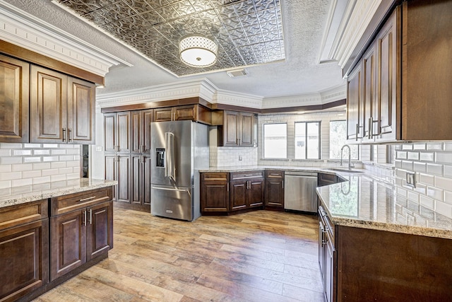 kitchen featuring backsplash, light stone counters, ornamental molding, stainless steel appliances, and light hardwood / wood-style flooring