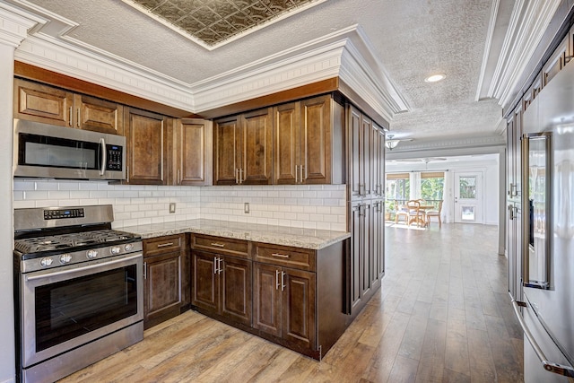 kitchen with backsplash, stainless steel appliances, light stone counters, and crown molding