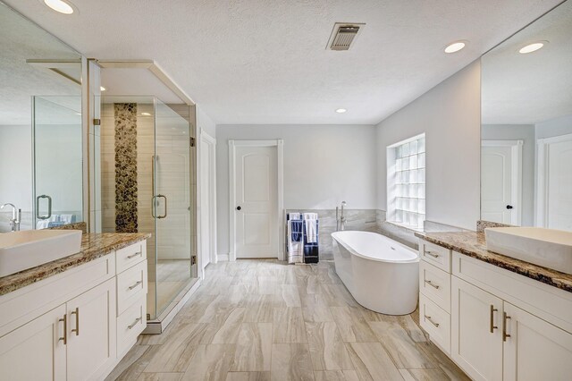 bathroom featuring separate shower and tub, tile walls, vanity, and a textured ceiling