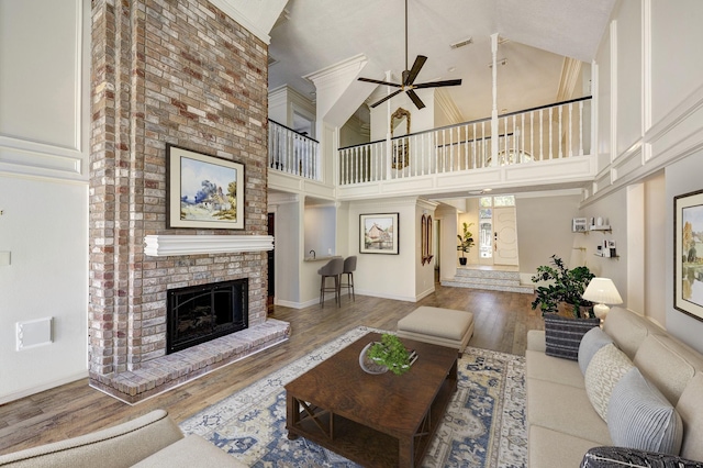 living room featuring ceiling fan, hardwood / wood-style floors, a towering ceiling, and a brick fireplace