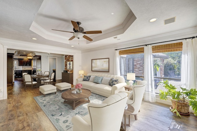 living room with wood-type flooring, crown molding, and a tray ceiling