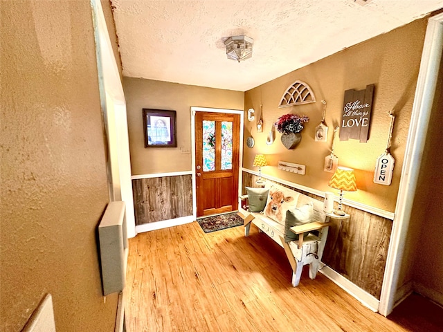 foyer entrance featuring wood-type flooring, a textured ceiling, radiator, and wood walls