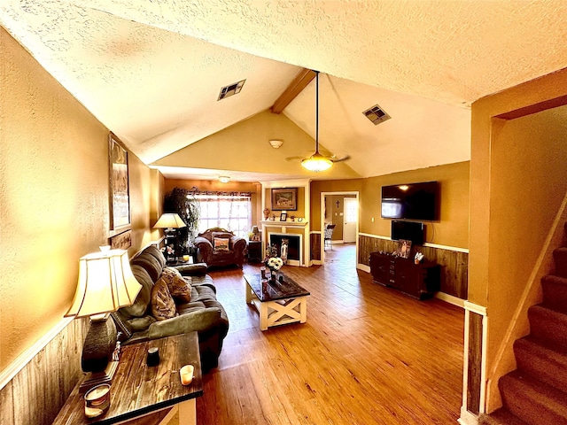 living room featuring vaulted ceiling with beams, wood walls, hardwood / wood-style floors, and a textured ceiling