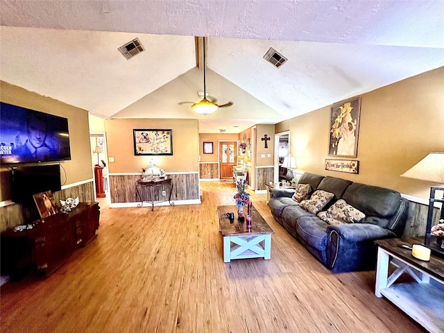 living room with lofted ceiling with beams, light wood-type flooring, a textured ceiling, and wooden walls