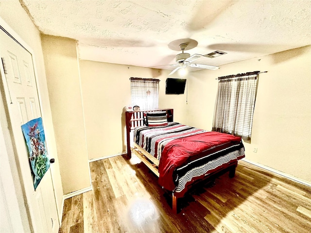 bedroom with ceiling fan, wood-type flooring, and a textured ceiling