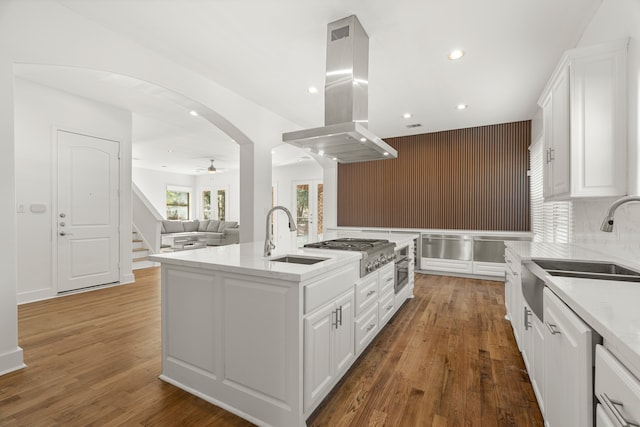 kitchen with sink, dark hardwood / wood-style floors, an island with sink, island range hood, and white cabinetry