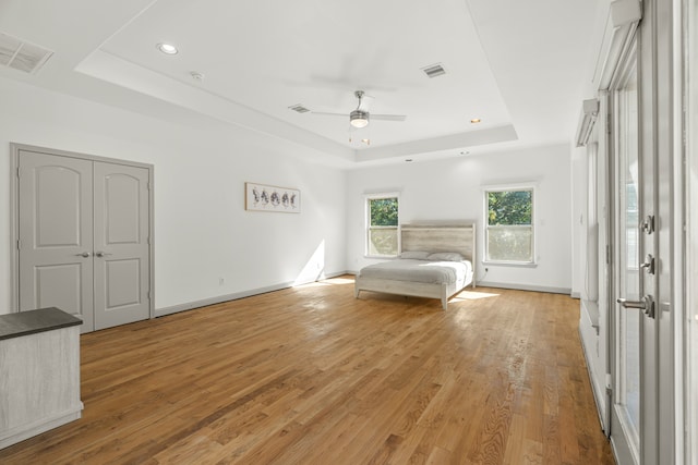 unfurnished bedroom featuring a tray ceiling, a closet, ceiling fan, and light hardwood / wood-style flooring