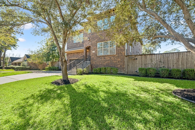 view of front of house featuring a front yard, concrete driveway, brick siding, and fence