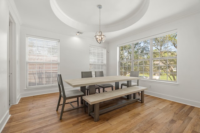 dining room featuring light hardwood / wood-style floors, a raised ceiling, ornamental molding, and a chandelier