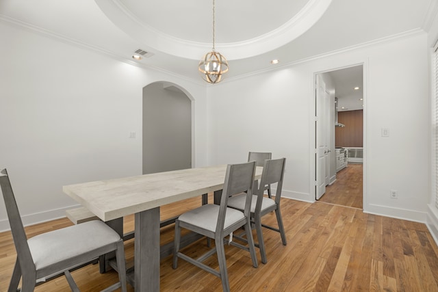 dining area featuring a tray ceiling, an inviting chandelier, light hardwood / wood-style floors, and ornamental molding