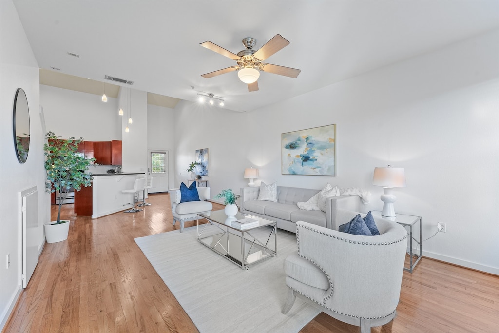 living room with ceiling fan, light hardwood / wood-style flooring, and a towering ceiling