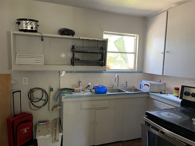 kitchen with electric range oven, white cabinetry, sink, and tasteful backsplash