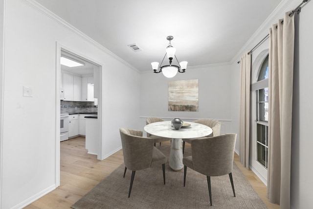 dining area featuring light wood-type flooring, ornamental molding, and an inviting chandelier