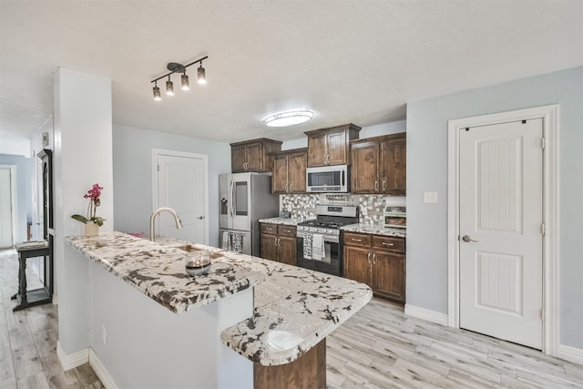 kitchen with stainless steel appliances, light hardwood / wood-style floors, a center island with sink, sink, and tasteful backsplash