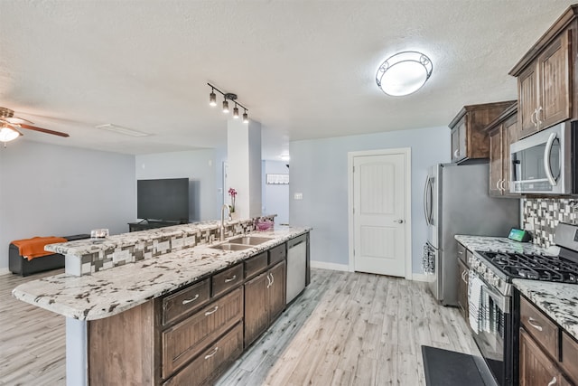 kitchen featuring light hardwood / wood-style floors, stainless steel appliances, a textured ceiling, sink, and a kitchen island with sink