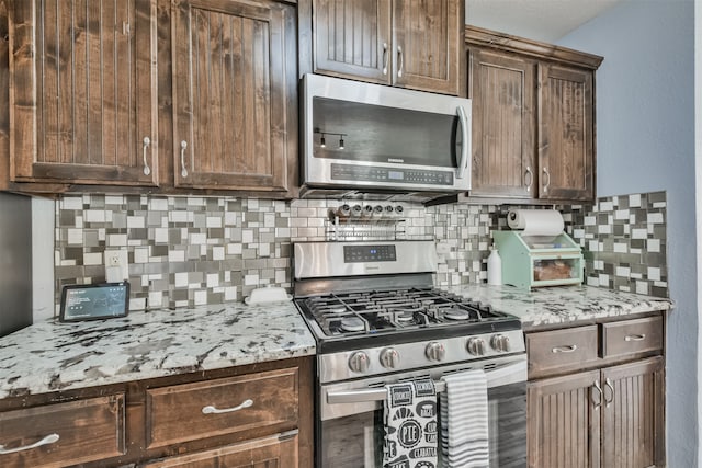 kitchen featuring stainless steel appliances, light stone countertops, dark brown cabinets, and tasteful backsplash