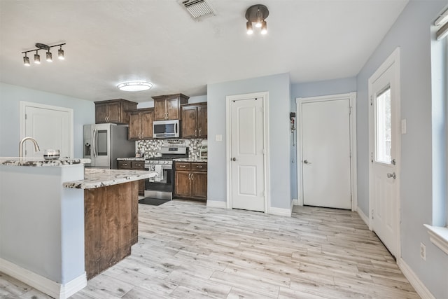 kitchen with stainless steel appliances, a center island with sink, light stone counters, backsplash, and light hardwood / wood-style flooring