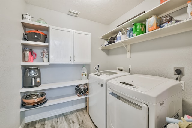 laundry area featuring a textured ceiling, light hardwood / wood-style flooring, washing machine and dryer, and cabinets