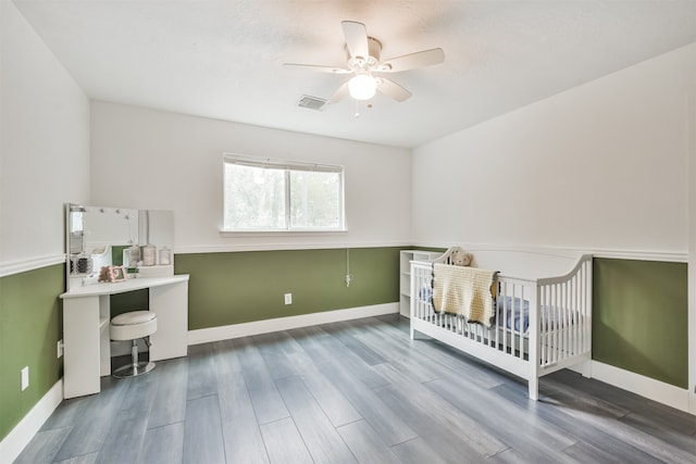 bedroom with hardwood / wood-style flooring, ceiling fan, and a nursery area