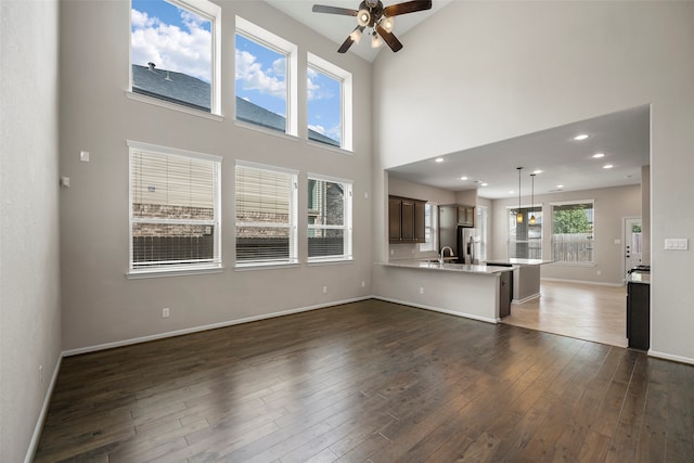 unfurnished living room featuring ceiling fan, a high ceiling, dark hardwood / wood-style floors, and sink