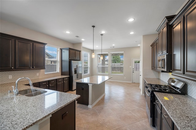 kitchen featuring sink, light stone counters, appliances with stainless steel finishes, a center island, and decorative backsplash