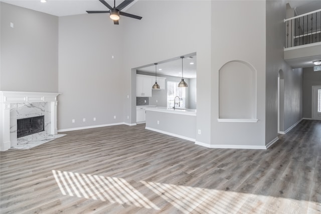 unfurnished living room featuring a high end fireplace, hardwood / wood-style floors, a towering ceiling, and ceiling fan