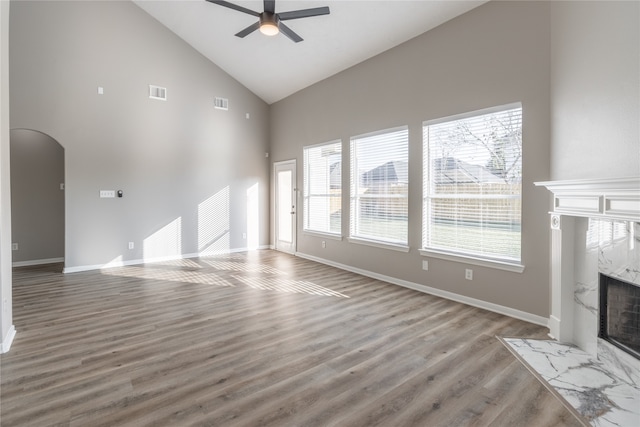 unfurnished living room featuring hardwood / wood-style flooring, ceiling fan, a high end fireplace, and high vaulted ceiling