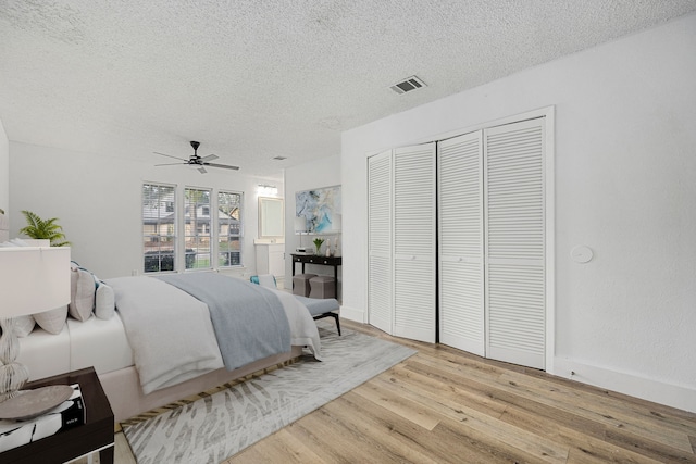 bedroom with a closet, a textured ceiling, ceiling fan, and light hardwood / wood-style flooring