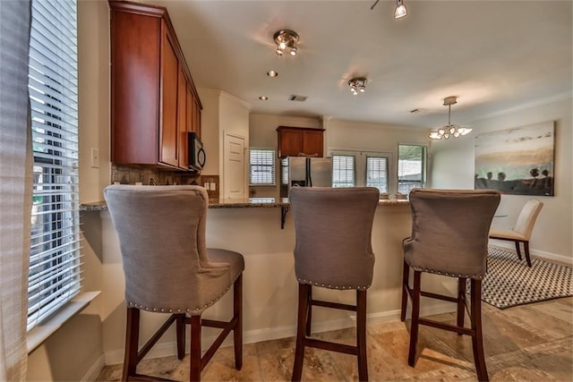 kitchen with ornamental molding, stainless steel fridge with ice dispenser, stone countertops, pendant lighting, and an inviting chandelier