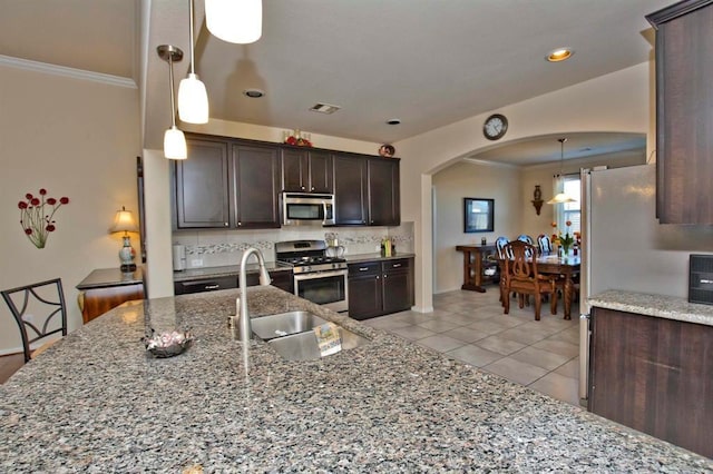 kitchen with pendant lighting, dark brown cabinetry, stainless steel appliances, sink, and light stone counters