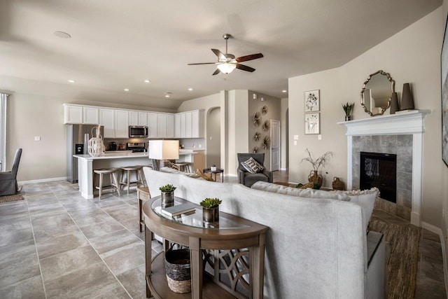 living room with a tile fireplace and ceiling fan