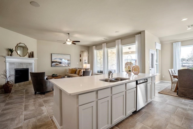 kitchen with a tile fireplace, dishwasher, sink, white cabinets, and a center island with sink