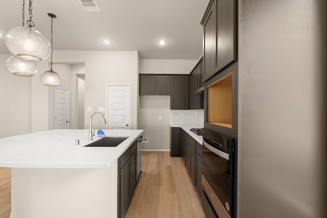 kitchen with light wood-type flooring, stainless steel appliances, a center island with sink, and sink