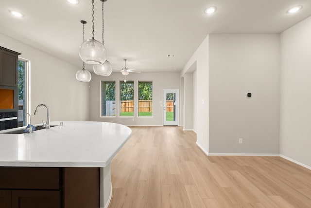 kitchen with dark brown cabinetry, light hardwood / wood-style floors, a center island with sink, ceiling fan, and pendant lighting