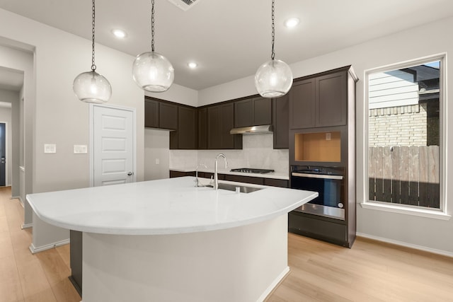 kitchen featuring light hardwood / wood-style floors, oven, a kitchen island with sink, and decorative backsplash