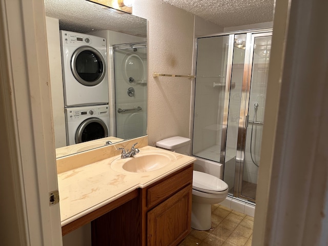 bathroom with stacked washer / drying machine, a textured ceiling, vanity, a shower with shower door, and toilet