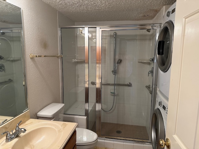 bathroom with toilet, a shower with door, a textured ceiling, vanity, and stacked washer / drying machine