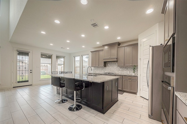 kitchen featuring light stone counters, stainless steel appliances, sink, a breakfast bar, and a kitchen island with sink