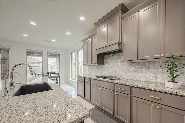 kitchen featuring stainless steel gas cooktop, sink, light stone counters, tasteful backsplash, and gray cabinets