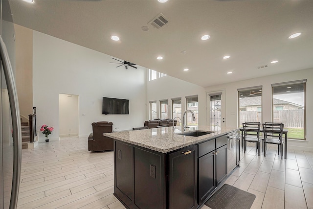 kitchen featuring a high ceiling, sink, light stone countertops, ceiling fan, and a kitchen island with sink