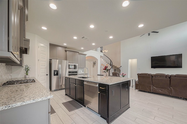 kitchen with stainless steel appliances, a center island with sink, sink, light stone counters, and backsplash